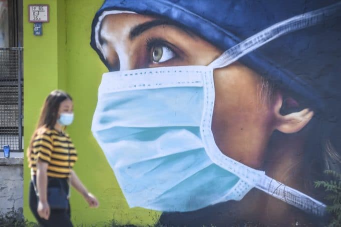 A woman wearing a protective mask walks by one of the murals dedicated to medical personnel of the Sacco infectious diseases hospital that fought the COVID-19, created by the artist Cosimo Cheone in Milan, Italy, Tuesday, July 21, 2020. (Claudio Furlan/LaPresse via AP)