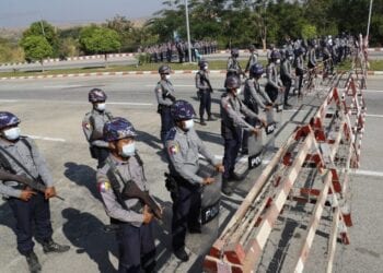 Policemen wearing protective face mask stand guard behind a road barricade, as a part of security preparations ahead of next week's opening of Myanmar's parliament in Naypyitaw, Myanmar, Friday, Jan. 29, 2021. Myanmar's election commission rejected allegations by the military that fraud played a significant role in determining the outcome of November's elections, which delivered a landslide victory to Aung San Suu Kyi's ruling party.(AP Photo/Aung Shine Oo)